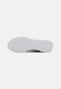 Valge spordijalatsite tald herringbone mustriga. Sile kummimaterjal. Peen brändi detail nähtav kanna lähedal. Puhtad ja modernsed jooned.