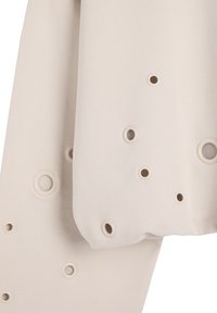 Beżowy materiał z okrągłymi wycięciami i kontrastującymi krawędziami, charakteryzujący się różnymi rozmiarami otworów dla tekstury i detali wzorniczych.