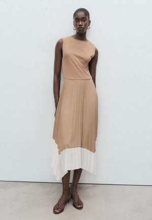 Sleeveless dress featuring a fitted brown bodice and a pleated, asymmetrical white hem. Styled with strappy brown sandals.