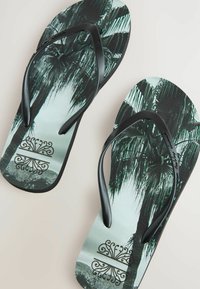 Sorte flip-flops med et palmeprint på grå såler, med teksturerede stropper og et dekorativt logo på bunden.