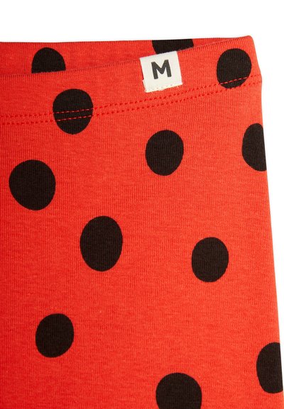 Red fabric with large black polka dots; features a white label with the letter "M" stitched on the waistband. Smooth texture.
