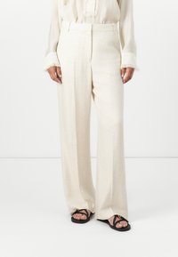 Celana panjang lebar berwarna beige yang terbuat dari campuran linen. Didesain dengan potongan ramping, memiliki lipatan di bagian depan, dan tekstur yang halus. Diperindah dengan pinggang yang sederhana.