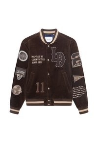 Brun kordflors varsityjacka med kontrasterande krämfärgade ränder, flera broderade lappar och text. Har tryckknappar och två sidofickor.