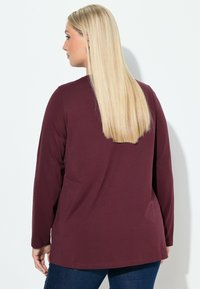 Pitkähihaine purppurapaita, jossa on pyöreä pääntie, rento istuvuus, pehmeästä kankaasta valmistettu, jossa on hieman kaareva helma ja takakappaleen muotoilu.