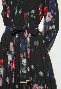 Robe plissée noire avec imprimé floral multicolore et ceinture à la taille ornée d'accents rectangulaires dorés.