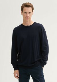 Granatowy sweter dzianinowy z długimi rękawami, okrągłym dekoltem i ściągaczami. Miękka tekstura, luźny fason, minimalny design bez wzorów lub akcentów.