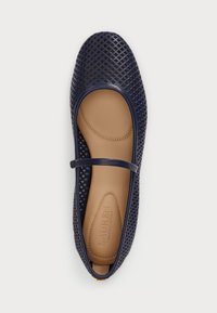 Sötétkék gumis lapos cipő, szőtt rácsos kialakítással, bokapánttal és sima világosbarna talppal, amelyen például a márka felirata van bajos. 