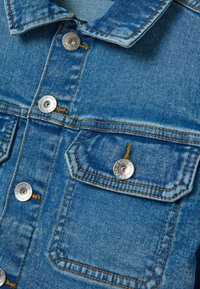 Blaue Jeansjacke mit silbernen Druckknöpfen, kontrastierend gelben Nähten und zwei Brusttaschen mit abgerundeten Klappen und strukturiertem Finish.