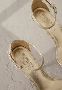 Gul strappy hælede sandaler med en skinnende læderfinish. Har en bred ankelrem og prægede mærkelabel på indersålen.