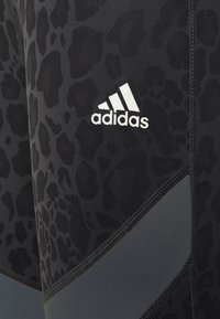 Pantaloni sportivi neri con stampa leopardata testurizzata, realizzati in un tessuto elastico, con logo Adidas riflettente e pannello grigio a contrasto.