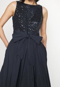 Ärmlös kvällsklänning med en paljettbelagd överdel i svart, en flödande mörk kjol och en knytbåge vid midjan.