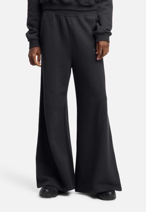 Czarne szerokie spodnie dresowe z wysokim stanem, wykonane z miękkiego materiału. Charakteryzują się gładką teksturą i subtelnym brandingiem.