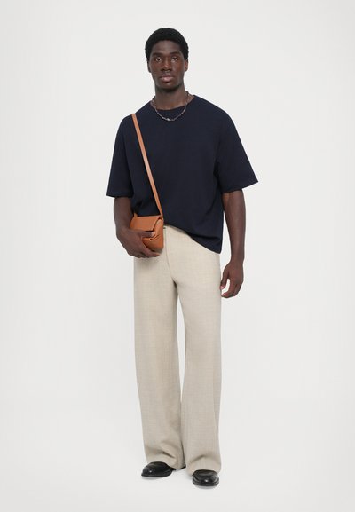 Ναυτική υπερμεγέθη μπλούζα, μπεζ φαρδιές παντελόνες, μαύρα παπούτσια, καφέ τσάντα χιαστί. Απαλή ύφασμα με χαλαρή εφαρμογή και μινιμαλιστικό σχέδιο.