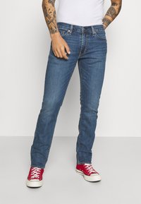 Jeans de mezclilla azul con un diseño de pernera recta, costuras visibles y estilo de cinco bolsillos, combinados con zapatos rojos.