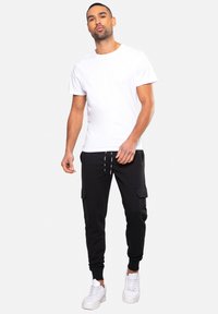 Witte katoenen t-shirt gecombineerd met zwarte cargobroek met zijzakken, geribbelde manchetten, en witte sneakers met dikke zolen.