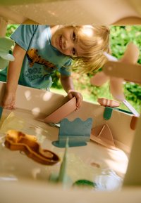 Πλαστικό τραπέζι παιχνιδιού με νερό σε ανοιχτό μπεζ χρώμα με πολύχρωμα αξεσουάρ: ροζ, μπλε και κίτρινες μορφές· υφές επιφανειών· σταγόνες νερού στις άκρες.