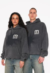 Sweatshirts à capuche en gris charbon, avec une poche avant et un logo blanc. Coupe douce et décontractée avec des poignets et un ourlet texturés en côtes.
