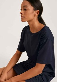 T-shirt blu navy a maniche corte con scollo rotondo e texture morbida, abbinato a una gonna coordinata. Design semplice e minimale, con linee pulite.