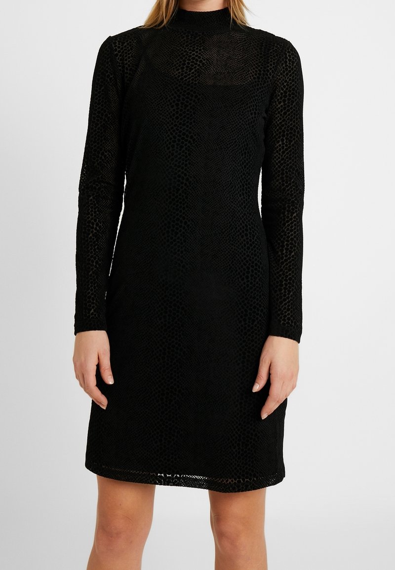 Robe noire cintrée à manches longues avec un motif texturé subtil, un col montant et un ourlet à hauteur du genou.