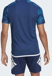 Granatowa sportowa koszulka z niebieskimi rękawami w wzory, zestawiona z dopasowanymi granatowymi szortami z białymi akcentami i geometrycznymi wzorami.