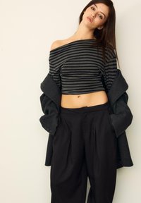 Čierny a šedý pruhovaný top bez ramienok skombinovaný s čiernymi nohavicami s vysokým pásom a tmavosivým kabátom s uvoľneným strihom.