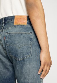 Vaqueros de mezclilla en azul claro con un parche de cuero que lleva "Levi Strauss & Co." en la parte trasera, dos bolsillos traseros con un diseño de costura distintivo.