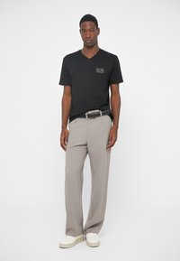 Μαύρο μπλουζάκι v-neck  με λογότυπο, συνδυασμένο με ανοιχτό γκρίζο παντελόνι καμπάνα και λευκά αθλητικά παπούτσια. Απλή, μοντέρνα και casual ενδυμασία.