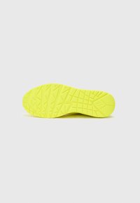 Semelle de chaussure jaune vif avec une surface texturée, présentant un motif de rainures angulaires et une légère courbure au niveau des orteils et du talon.