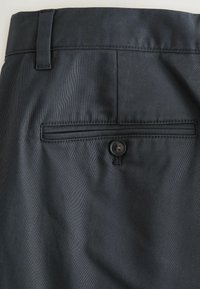 Pantalon habillé gris foncé en gros plan montrant une poche arrière avec fermeture par bouton et passants de ceinture à la taille.