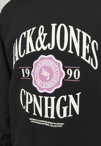 Zwarte sweatshirt met grote witte tekst "JACK & JONES" en een paarse zegel met "CPNHGN ORIGINALS CLUB SINCE 1990," met een standaard pasvorm en katoen stof.