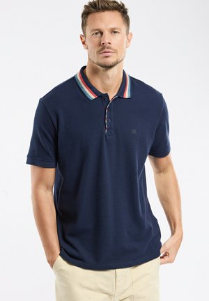 Polo bleu marine avec un col rayé multicolore, deux boutons, manches courtes, et un petit logo sur la poitrine, présentant une texture lisse.
