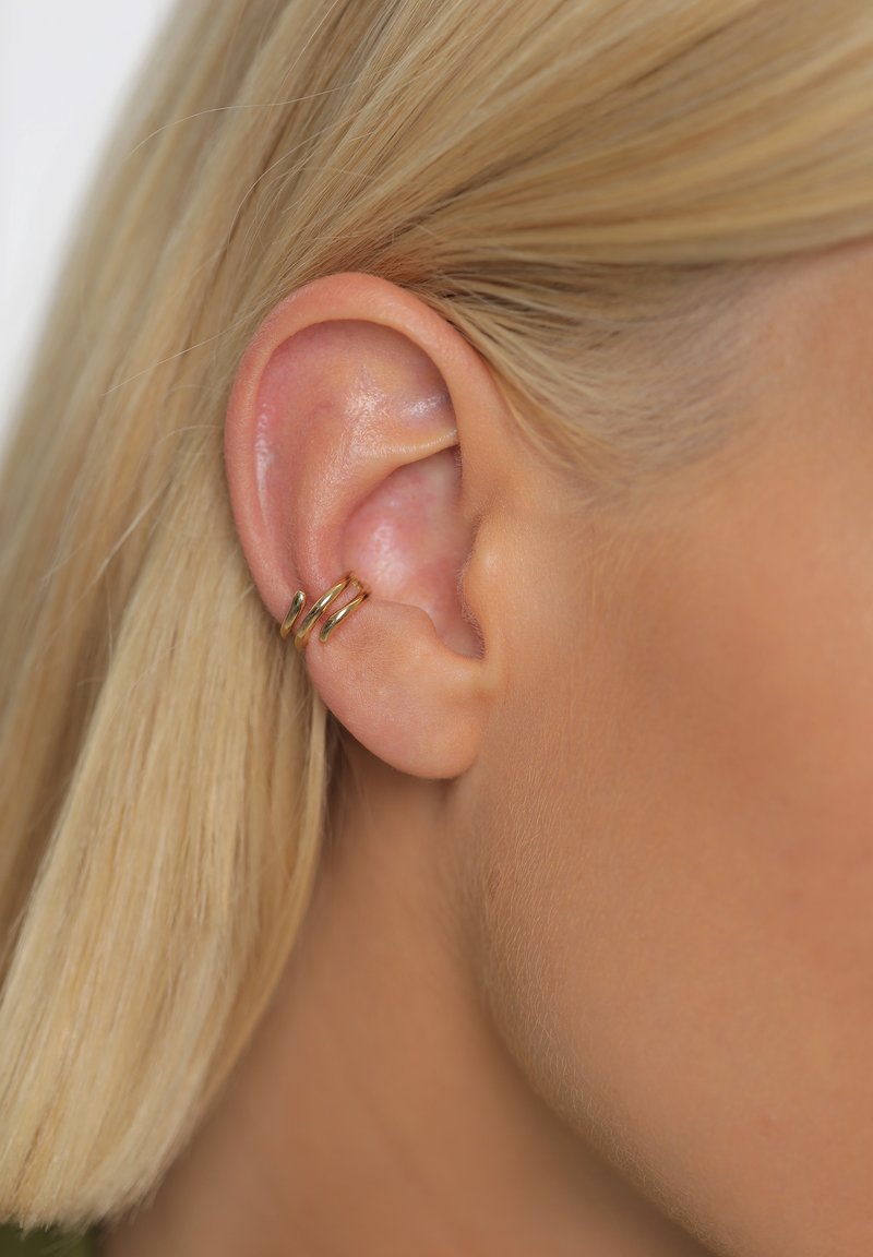 Gros plan de l'oreille d'une femme blonde avec deux petits anneaux dorés sur le cartilage externe.