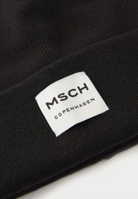 Beanie lavorato a maglia nero con un'etichetta bianca con testo nero, che legge "MSCH COPENHAGEN", cucita sul lato del cappello.