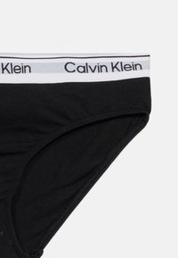 Μαύρα εσώρουχα Calvin Klein με λευκή ζώνη μέσης που φέρει το λογότυπο Calvin Klein σε μαύρο κείμενο σε μονόχρωμο φόντο.