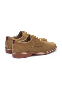 Des chaussures en daim marron avec un design à lacets, un bout rond et un accent de talon rougeâtre. Semelle plate en caoutchouc avec des détails de couture.