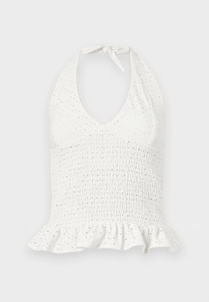 Bílý krátký top s halter výstřihem, našitým žabičkováním, děrovanými detaily a volánkovým lemem na jednoduchém pozadí.