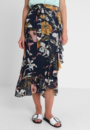 Marineblå blomster printet slå-om nederdel med flæsekant og bindebånd i taljen, båret med mintgrøn top og hvide slid-sandaler med spænder.