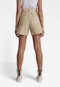 Béžové šortky s vysokým pasem a na míru střiženým střihem, dvěma zadními kapsami a detaily švů, doplněné bílými kotníkovými botami.