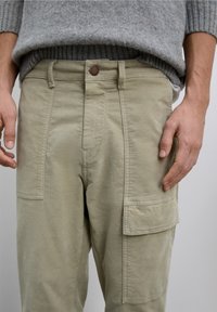 Pantalones cargo beige con bolsillos laterales, cierre de botones y un ajuste ligeramente holgado, confeccionados en tejido de algodón suave y texturizado.