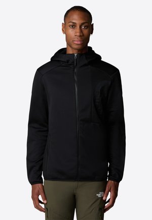 Black zip-up hoodie with a textured finish, front pocket, and a hood. Features a logo on the chest and is paired with olive green pants.