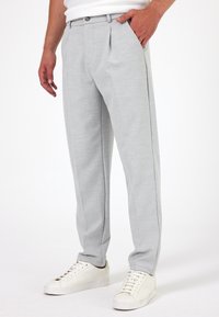 Lichtgrijze broek met een gestructureerde weving en voorplooien, voorzien van een knoopsluiting en twee zijzakken, gecombineerd met witte sneakers.