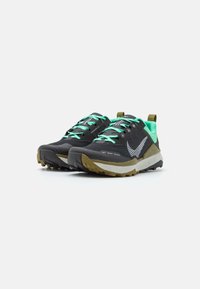 Zwarte trailschoenen met een gestructureerde bovenkant, groene veters en reflecterende accenten. Beschikt over een stevige zool voor grip en een groene hielstrook.