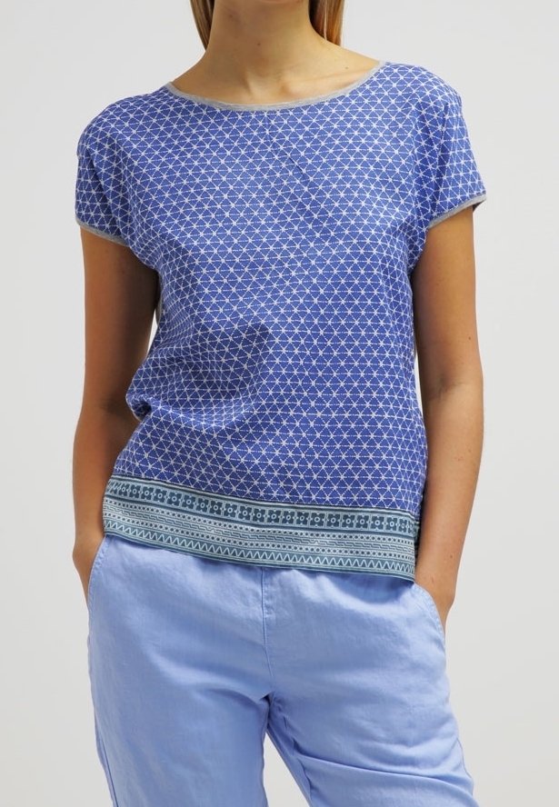 Top azul de manga corta con un patrón geométrico y un dobladillo estampado a contraste. La tela parece ligera y ligeramente texturizada.