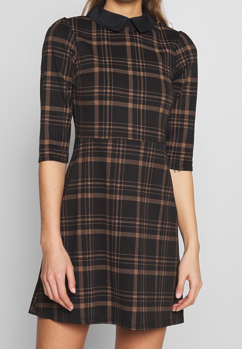 Svart rutig klänning med bruna och beiga linjer, med svart krage, trekvartsärmar och en utsvängd kjoldesign.