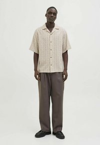 Lühikeste varrukatega beež triiksärk teemantmustriga, ees nööbitav, kombineeritud lahtiste pruunide pükstega ja mustade kingadega.