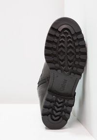 Botín negro de cuero con suela de goma texturizada, cremallera lateral y logo en relieve, que presenta un patrón de tracción robusto para mejor agarre.