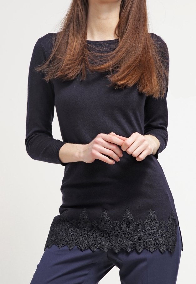 Marinblå långärmad topp med en texturerad svart spetskant, med en rund halsringning och figurnära silhuett. Slätt stickat tyg.
