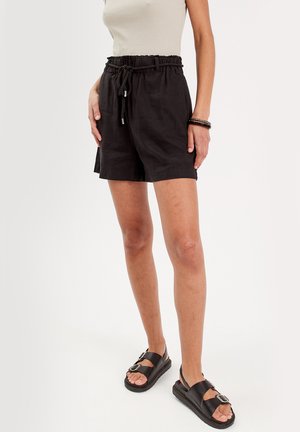 Pantaloni shorts neri in lino con vita elasticizzata e cordino, dotati di tasche laterali e un fit rilassato, abbinati a sandali neri.
