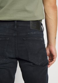 Mörkblå jeans i ett hållbart tyg, med en svart läderlapp vid midjan och dubbelsydda bakfickor.