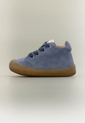 Chaussure en daim bleu pour tout-petit avec lacets bleu foncé et semelle en caoutchouc marron sur fond gris clair uni.